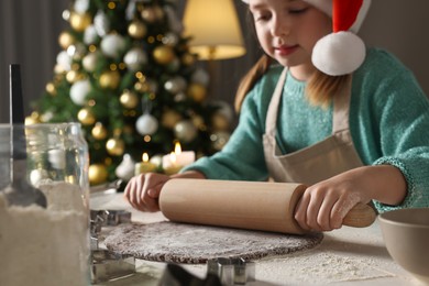 Cute little girl in Santa hat making Christmas cookies at home, focus on rolling pin