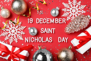 Photo of Text 19 December Saint Nicholas Day and festive decor on red background, flat lay