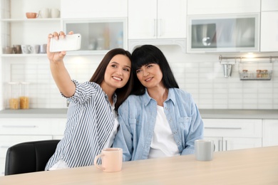 Young woman and her mature mother taking selfie at table indoors