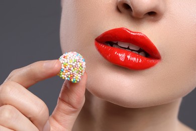 Photo of Young woman with beautiful red lips makeup eating candy on grey background, closeup