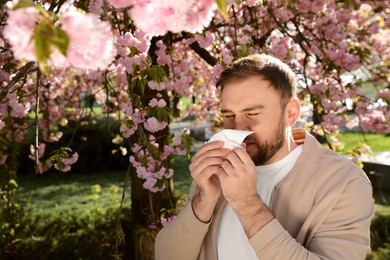 Man suffering from seasonal pollen allergy near blossoming tree outdoors