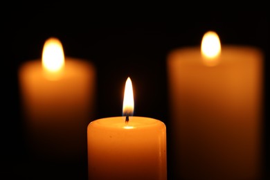 Photo of Burning wax candles on black background, closeup
