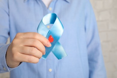 Woman holding light blue ribbon with paper blood drop, closeup. World Diabetes Day