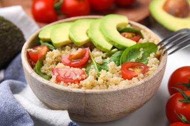 Photo of Delicious quinoa salad with tomatoes, avocado slices and spinach leaves served on table, closeup