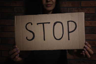 Young woman with sign STOP near brick wall, closeup. Domestic violence concept
