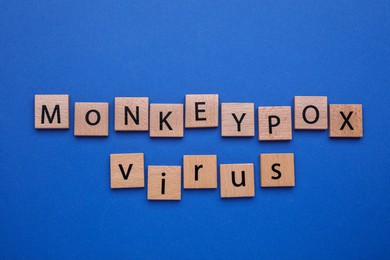 Photo of Words Monkeypox Virus made of wooden squares on blue background, flat lay