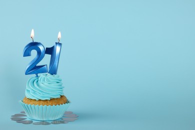 Delicious cupcake with number shaped candles on light blue background, space for text. Coming of age party - 21th birthday