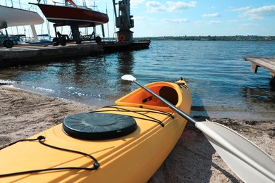 Yellow kayak with paddle on beach near river, closeup. Summer camp activity