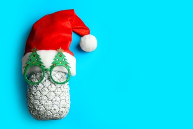 Top view of pineapple with Santa hat and Christmas glasses on light blue background, space for text. Creative concept