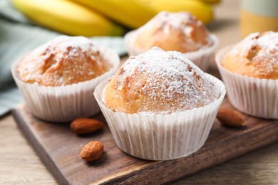 Photo of Tasty muffins powdered with sugar on wooden table, closeup