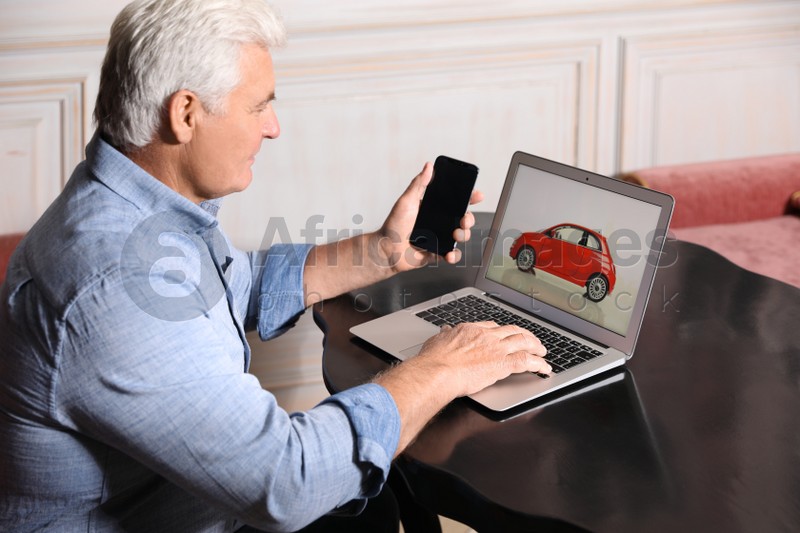 Man using laptop and phone to buy car at table indoors