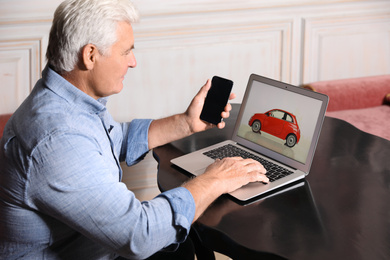 Man using laptop and phone to buy car at table indoors