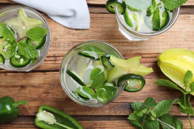 Photo of Glasses of spicy cocktail with jalapeno, carambola and mint on wooden table, flat lay