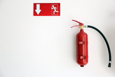 Fire extinguisher and emergency exit sign on white wall, space for text
