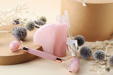 Photo of Composition with rose quartz gua sha tool, facial roller and bottle of serum on beige background