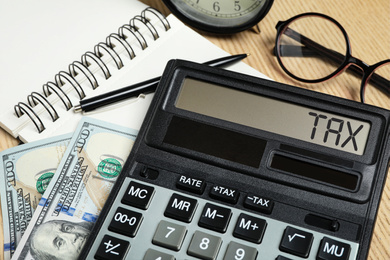 Calculator with word Tax, money and stationery on table, closeup