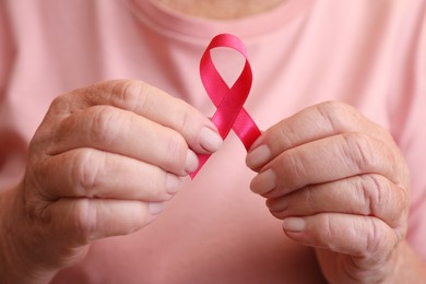Senior woman holding pink ribbon, closeup. Breast cancer awareness