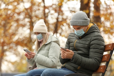 People in medical masks keeping distance while sitting on bench outdoors. Protective measures during coronavirus quarantine