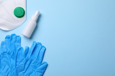 Hand sanitizer, medical gloves and respirator on light blue background, flat lay. Space for text