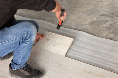 Professional worker using hammer during installation of new laminate flooring, closeup. Space for text
