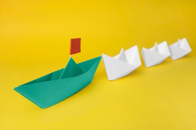 Photo of Group of paper boats following green one on yellow background. Leadership concept