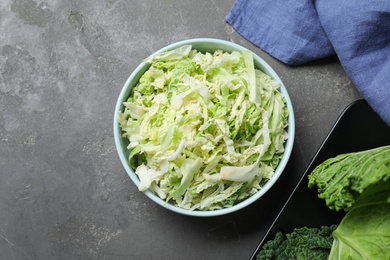 Photo of Cut fresh savoy cabbage in bowl on grey table, flat lay