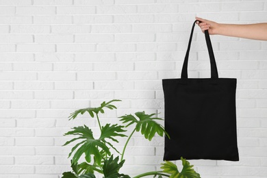 Woman holding eco bag near green plant and brick wall. Mock up for design
