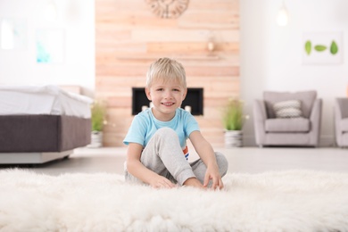 Cute little boy sitting on fur rug at home