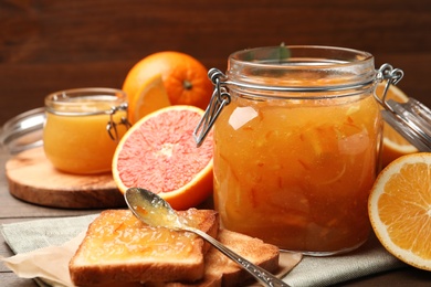 Delicious orange marmalade in jar, fresh fruits and toasts on table