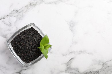 Black sesame seeds and green leaf in glass bowl on white marble table, top view. Space for text