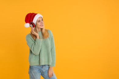 Happy woman with headphones on yellow background, space for text. Christmas music