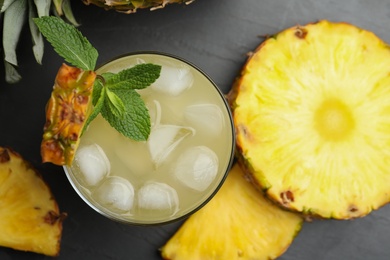 Photo of Delicious pineapple juice with fresh fruit and mint on black table, flat lay
