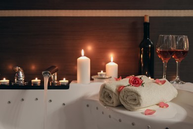 Glasses of wine, towels, candles and rose on tub in bathroom. Romantic atmosphere