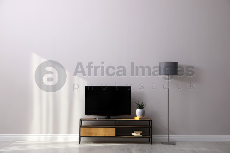 Photo of Elegant room interior with TV on cabinet and lamp near light wall