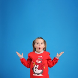 Surprised little girl in Christmas sweater on blue background, space for text