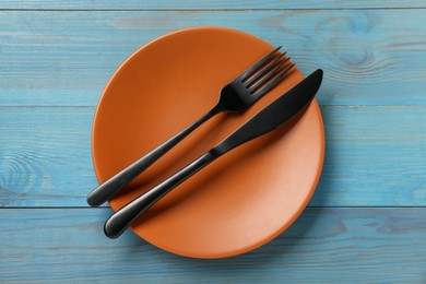 Orange ceramic plate with cutlery on light blue wooden table, top view