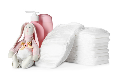 Stack of disposable diapers, toy bunny and toiletries on white background