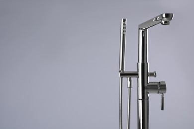 Modern bathtub faucet with hand shower on grey background. Space for text