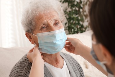 Doctor putting protective mask on senior woman at nursing home