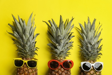 Pineapples with sunglasses on yellow background, flat lay. Creative concept