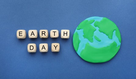 Phrase Earth Day made with wooden cubes and planet model on blue background, flat lay