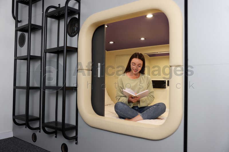 Happy young woman reading book in capsule of pod hostel