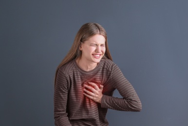 Young woman having heart attack on gray background