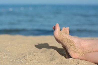 Child resting on sand near sea, closeup of feet. Space for text
