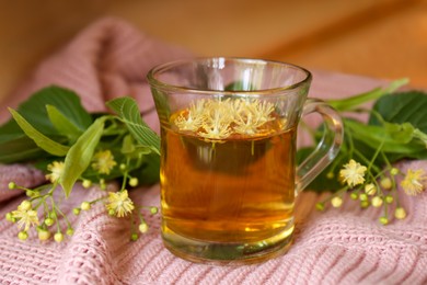 Photo of Glass cup of aromatic tea with linden blossoms on pink cloth, closeup