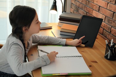 Little girl doing homework with modern tablet at home, focus on hand