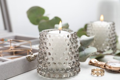 Burning candle and jewelry box with beautiful bijouterie on white wooden table, closeup