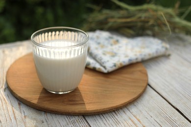 Glass of tasty fresh milk on white wooden table outdoors, space for text
