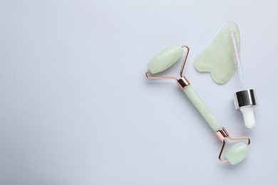 Gua sha stone, face roller and dropper on light background, flat lay. Space for text