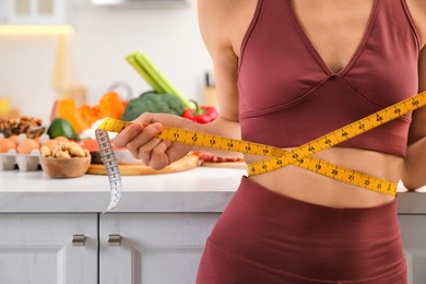 Woman with measuring tape in kitchen, closeup. Keto diet